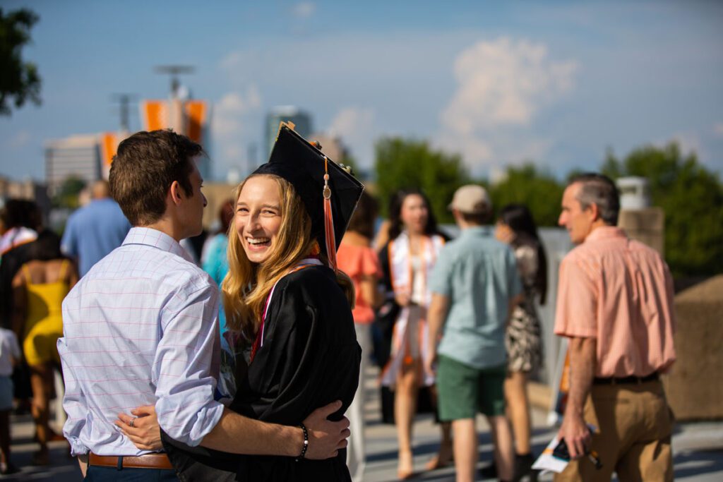 A graduate smiles while hugging another person after commencement.